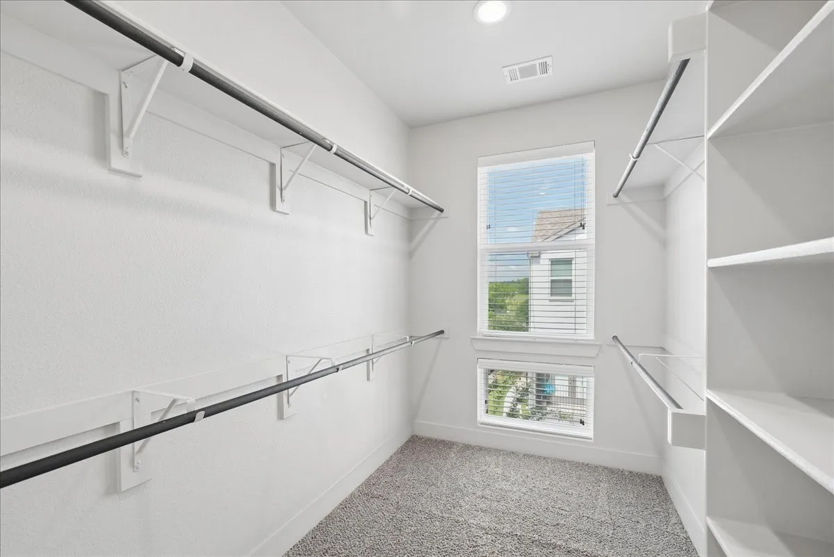 Spacious walk-in closet featuring white built-in shelving, multiple hanging rods, and two windows with blinds