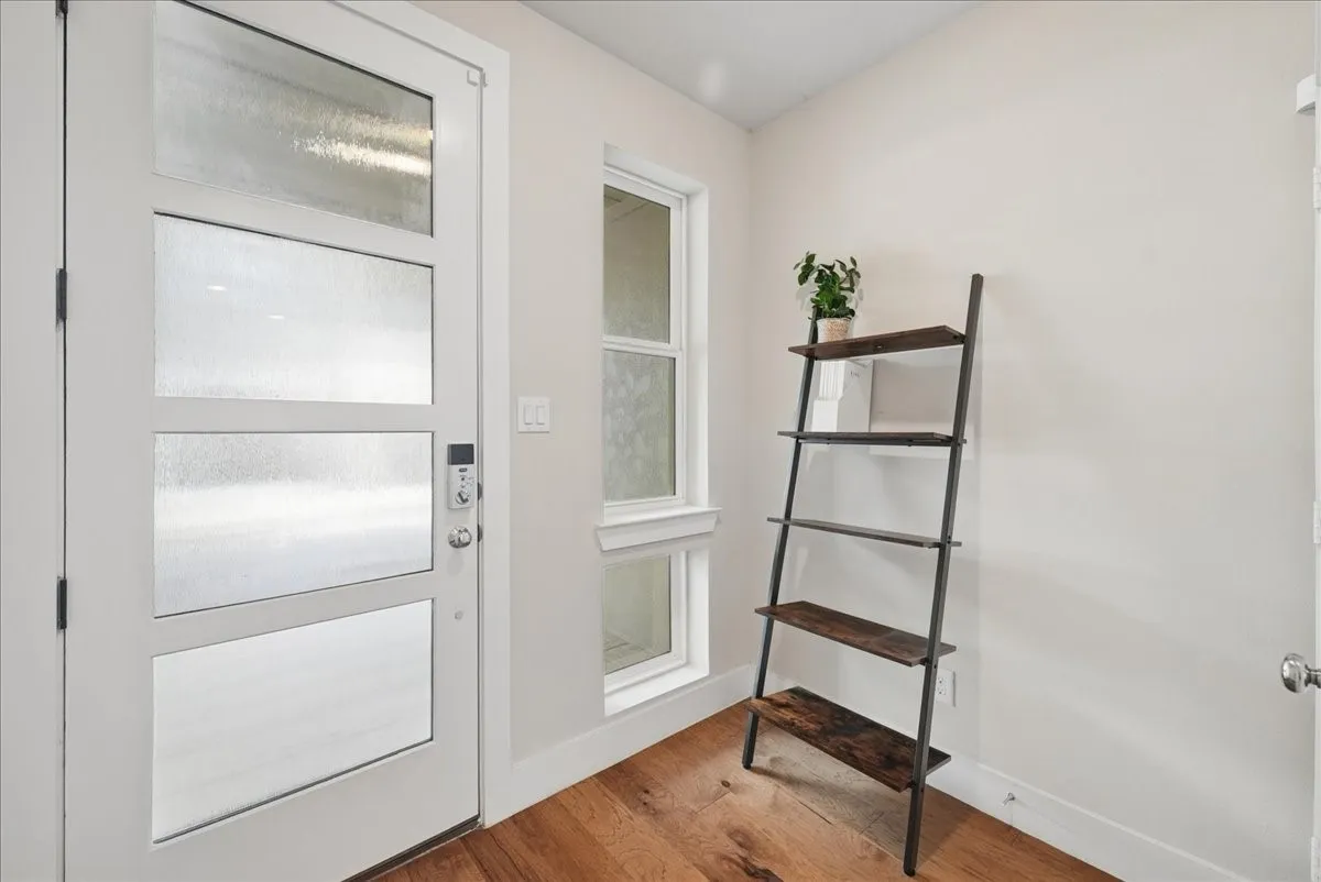 Contemporary entry door with frosted panels, smart lock hardware, wood-finish flooring, and a large vertical window