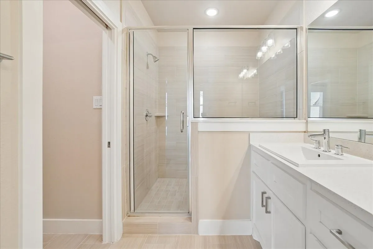 Glass-enclosed shower with tiled walls and floor, single vanity with integrated sink, chrome fixtures, and overhead recessed lighting