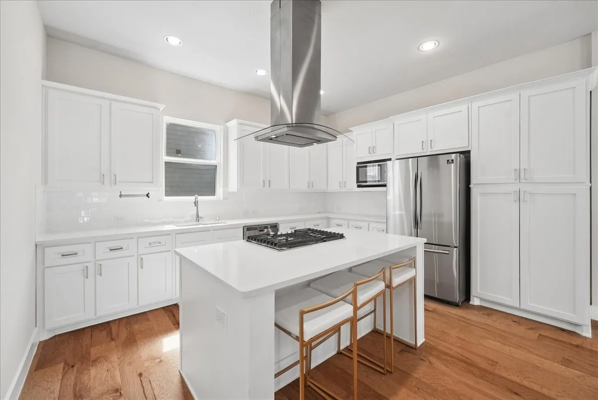 White shaker cabinetry with ample storage, stainless steel appliances, a center island with cooktop, and wood-finish flooring