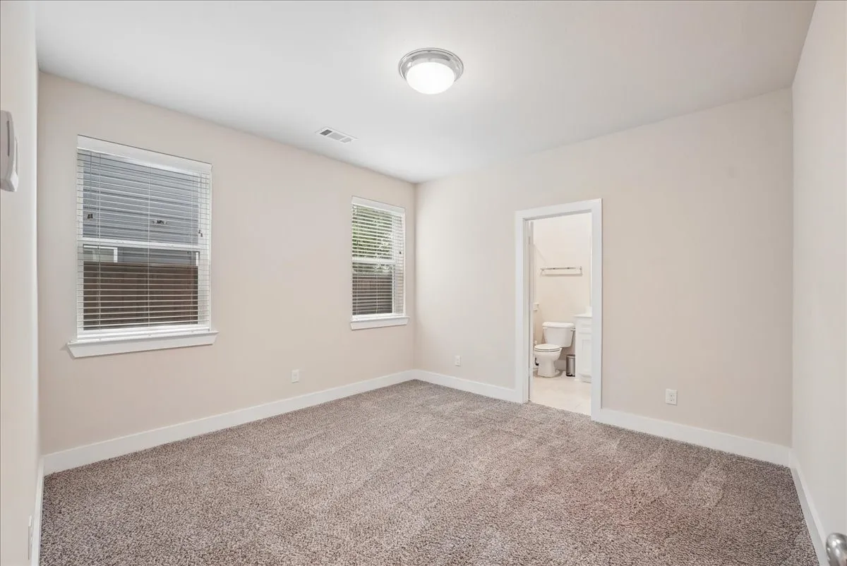 Carpeted room featuring two windows with blinds, a flush mount ceiling light, and direct access to a separate bathroom