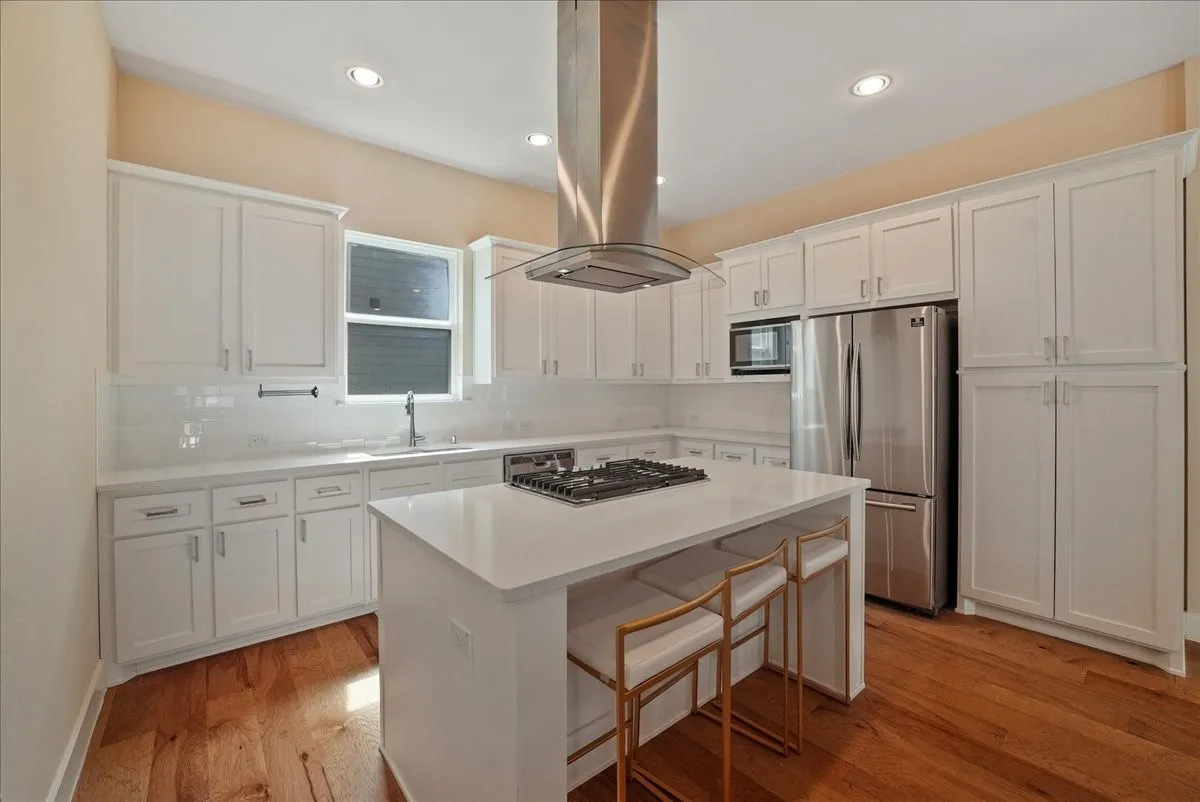 Kitchen featuring white cabinetry, stainless steel appliances, a center island with a gas cooktop, and wood-finish flooring