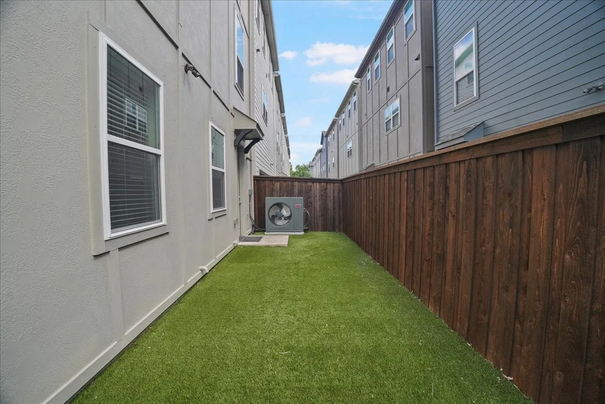 Private outdoor space featuring artificial turf, a wood privacy fence, and an exterior air conditioning unit
