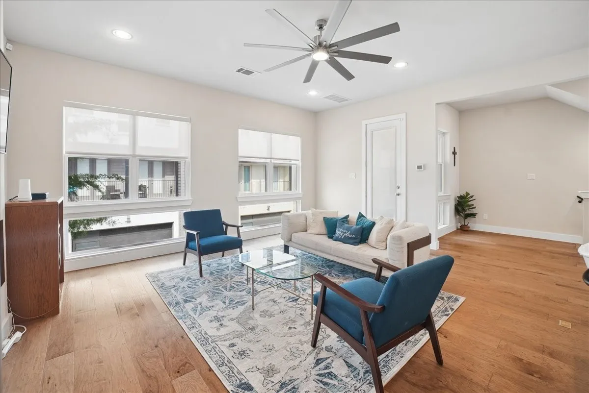 Recessed lighting, wood-finish flooring, ceiling fan, multiple windows with roller shades, and a white paneled door