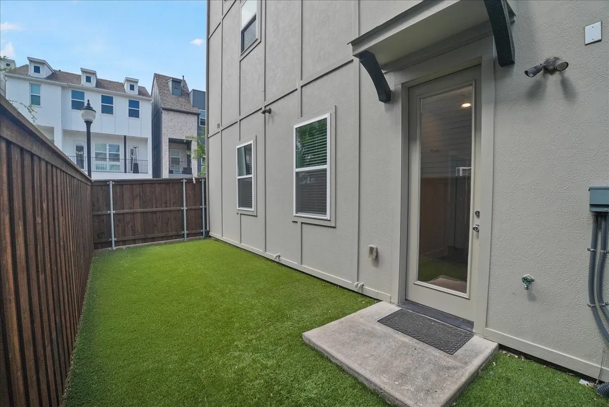 Enclosed backyard with artificial turf, wood fencing, and a glass-paneled exterior door