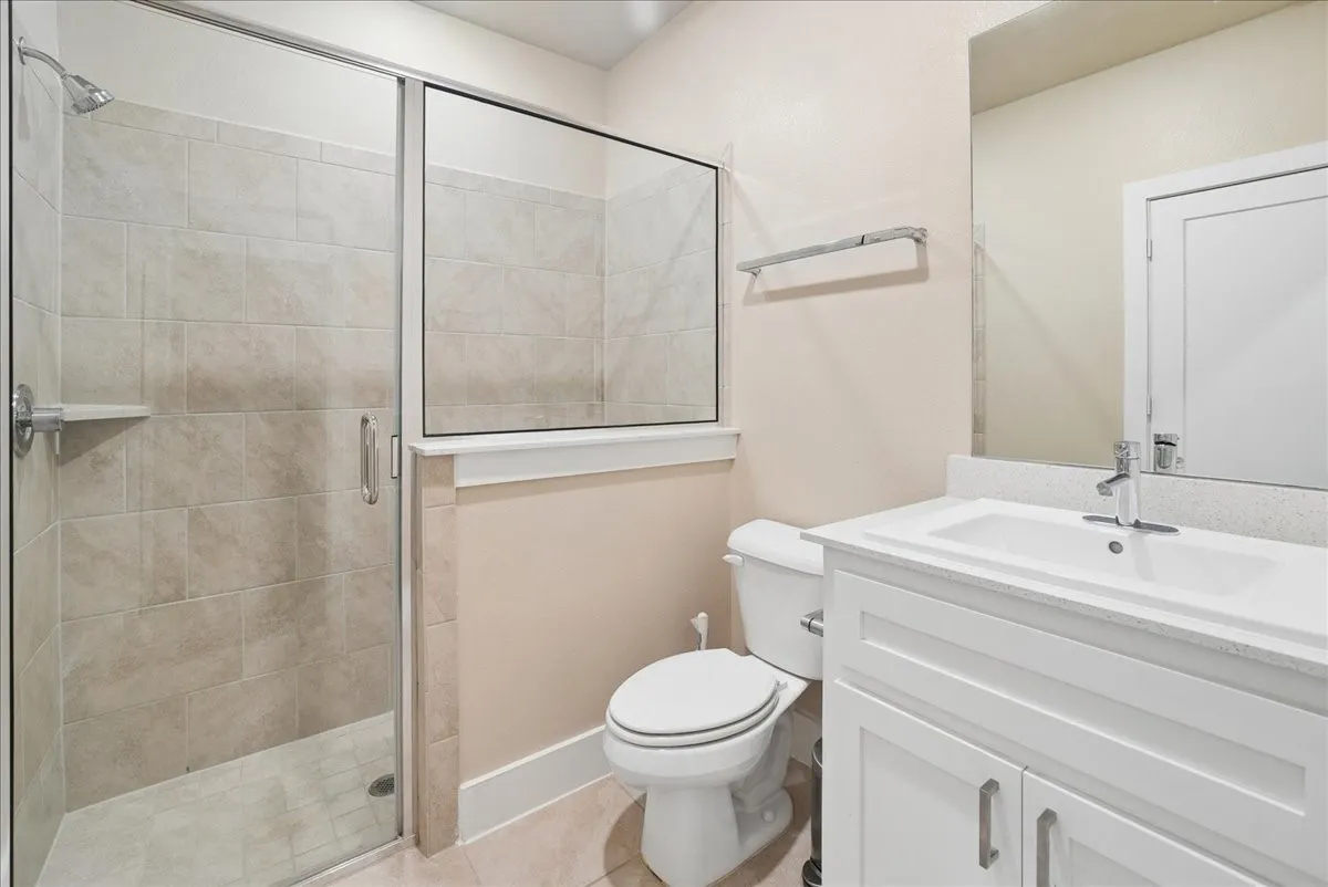 Glass-enclosed shower with tile surround, white vanity with integrated sink, and a framed mirror