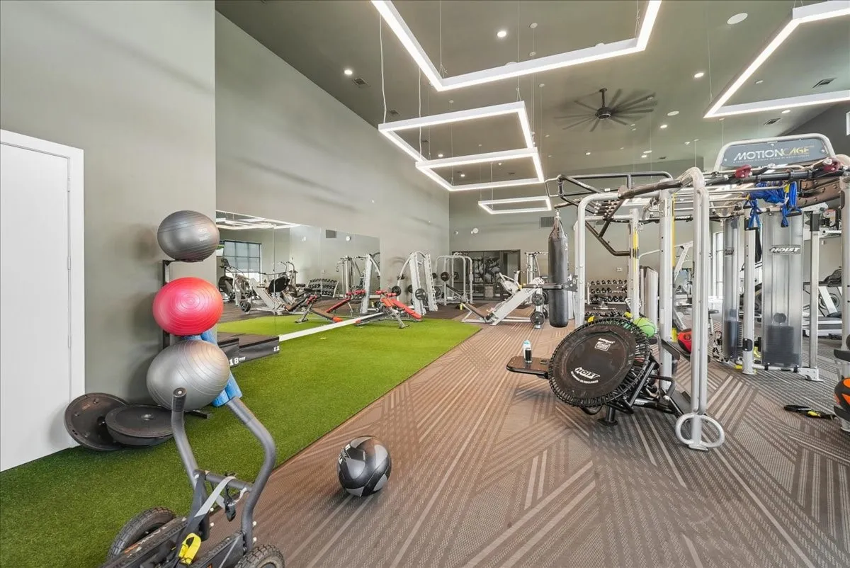 Gym space featuring high ceilings, turf flooring, mirrored walls, and geometric pattern carpeting