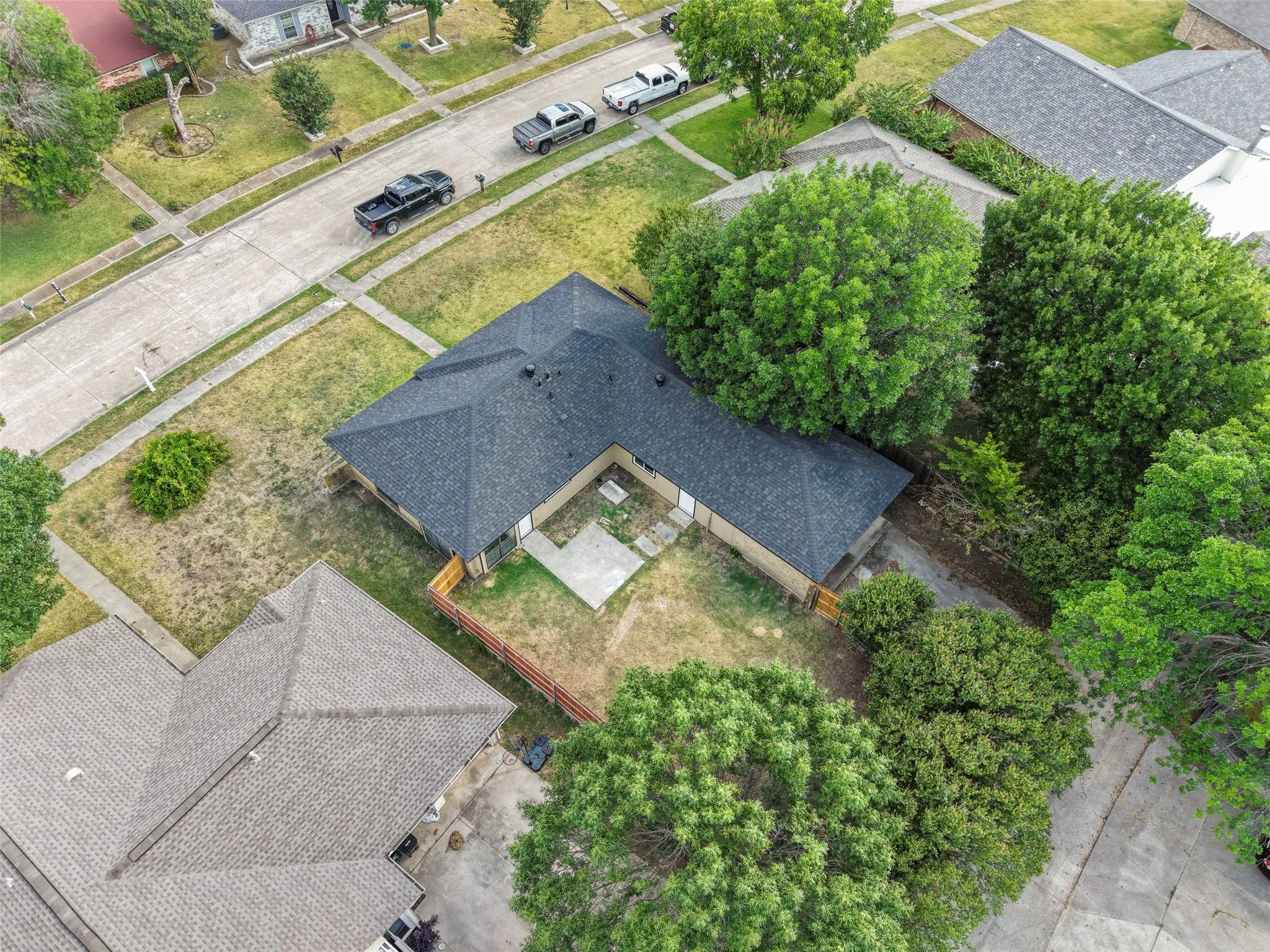 Dark shingle roof, mature trees, concrete patios, and wood fencing