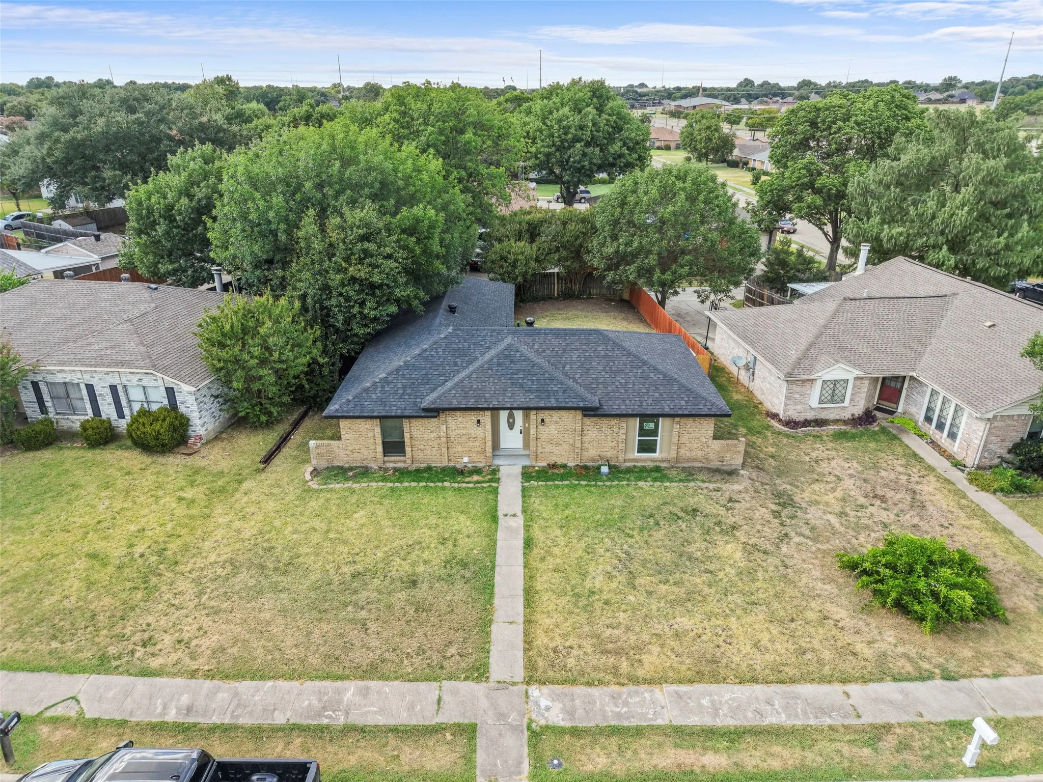 Brick exterior, dark shingle roof, concrete walkway, landscaped front, mature trees