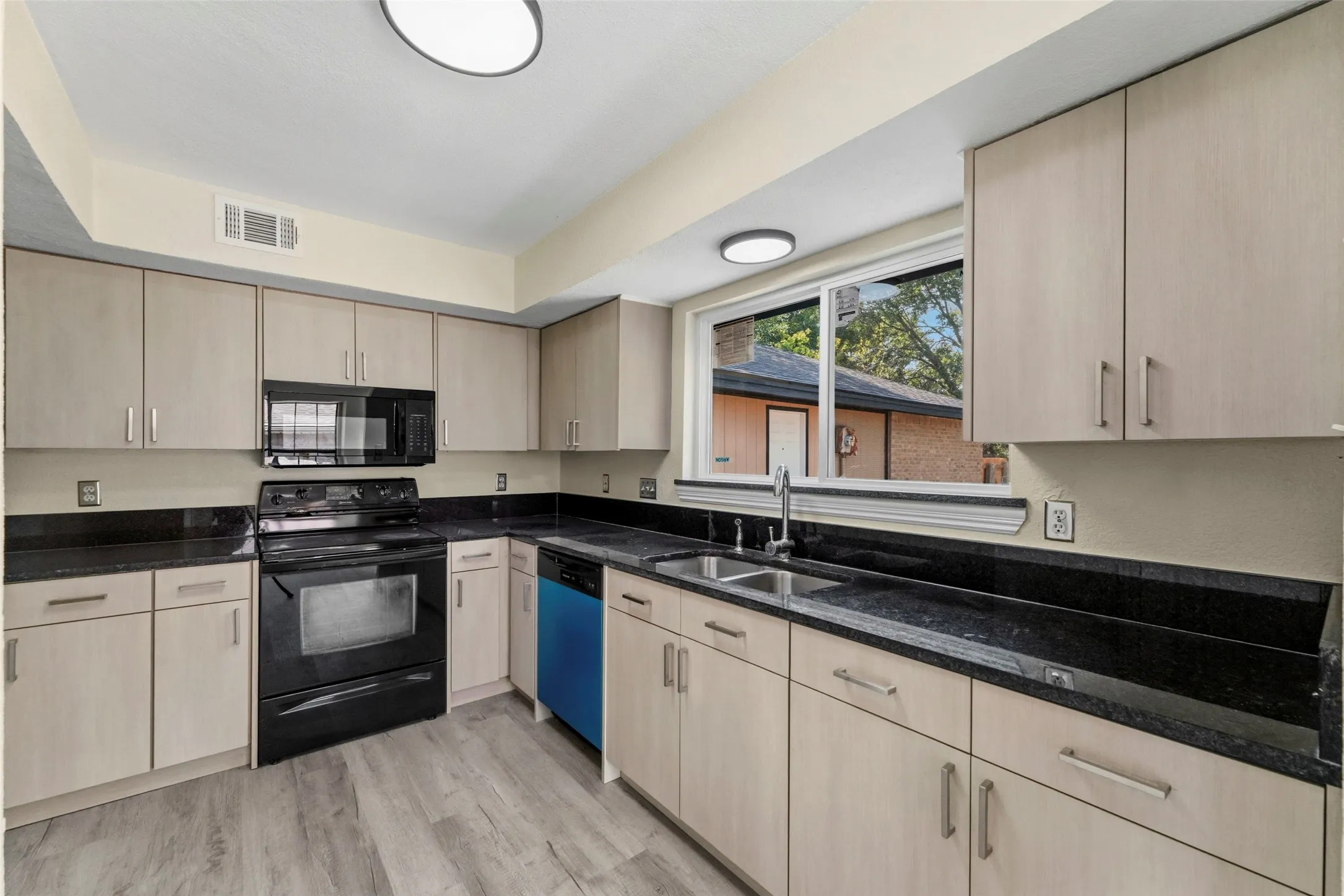 Wood-finish flooring with light-toned cabinetry, dark countertops, and stainless steel sink