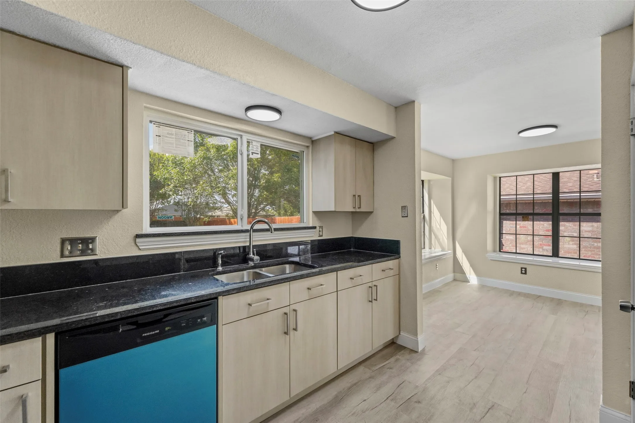 Kitchen featuring a double basin stainless steel sink, black countertops, and light-toned cabinetry