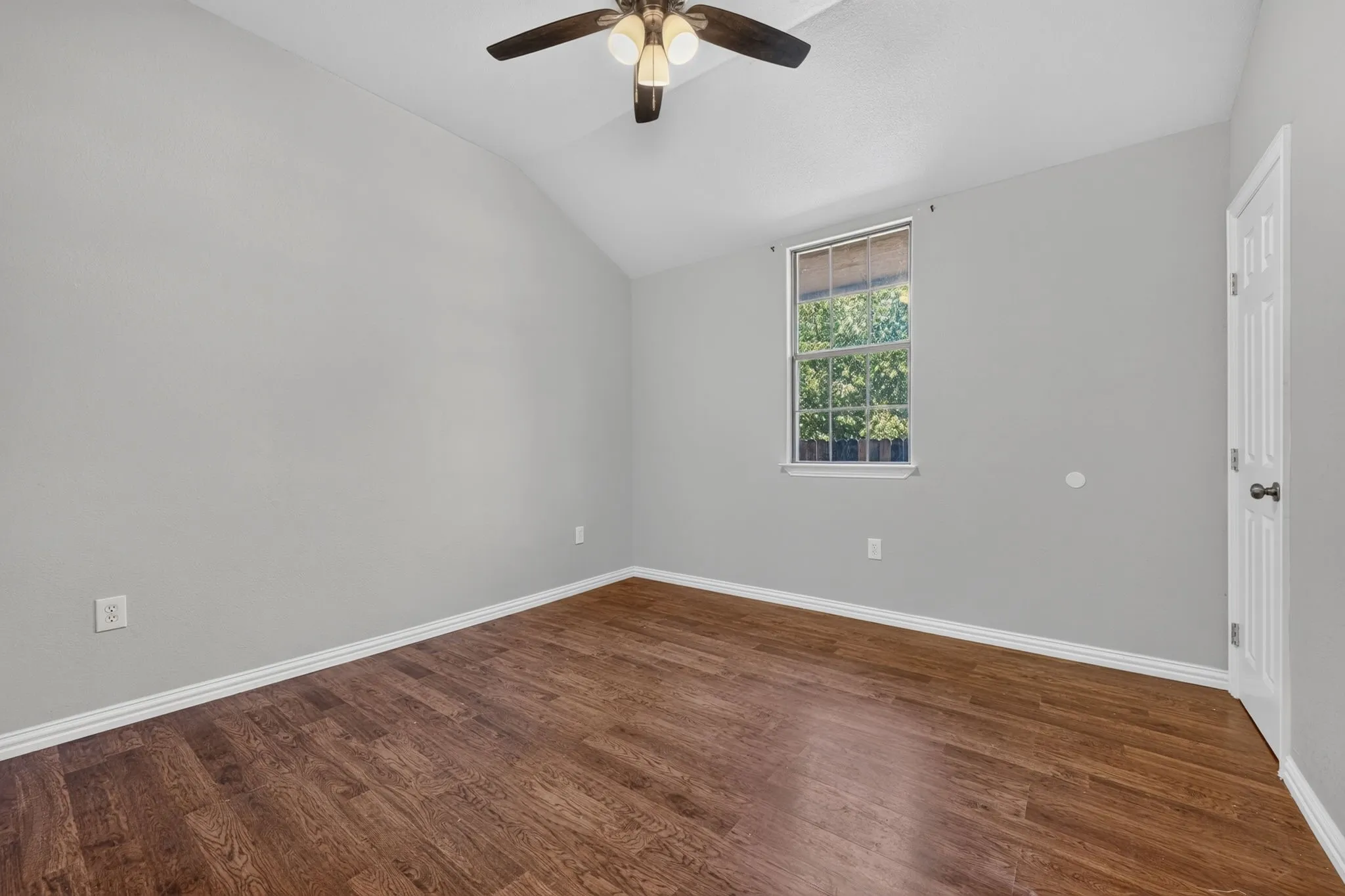 Vaulted ceiling, wood-look finish flooring, ceiling fan, natural light, and a paneled interior door