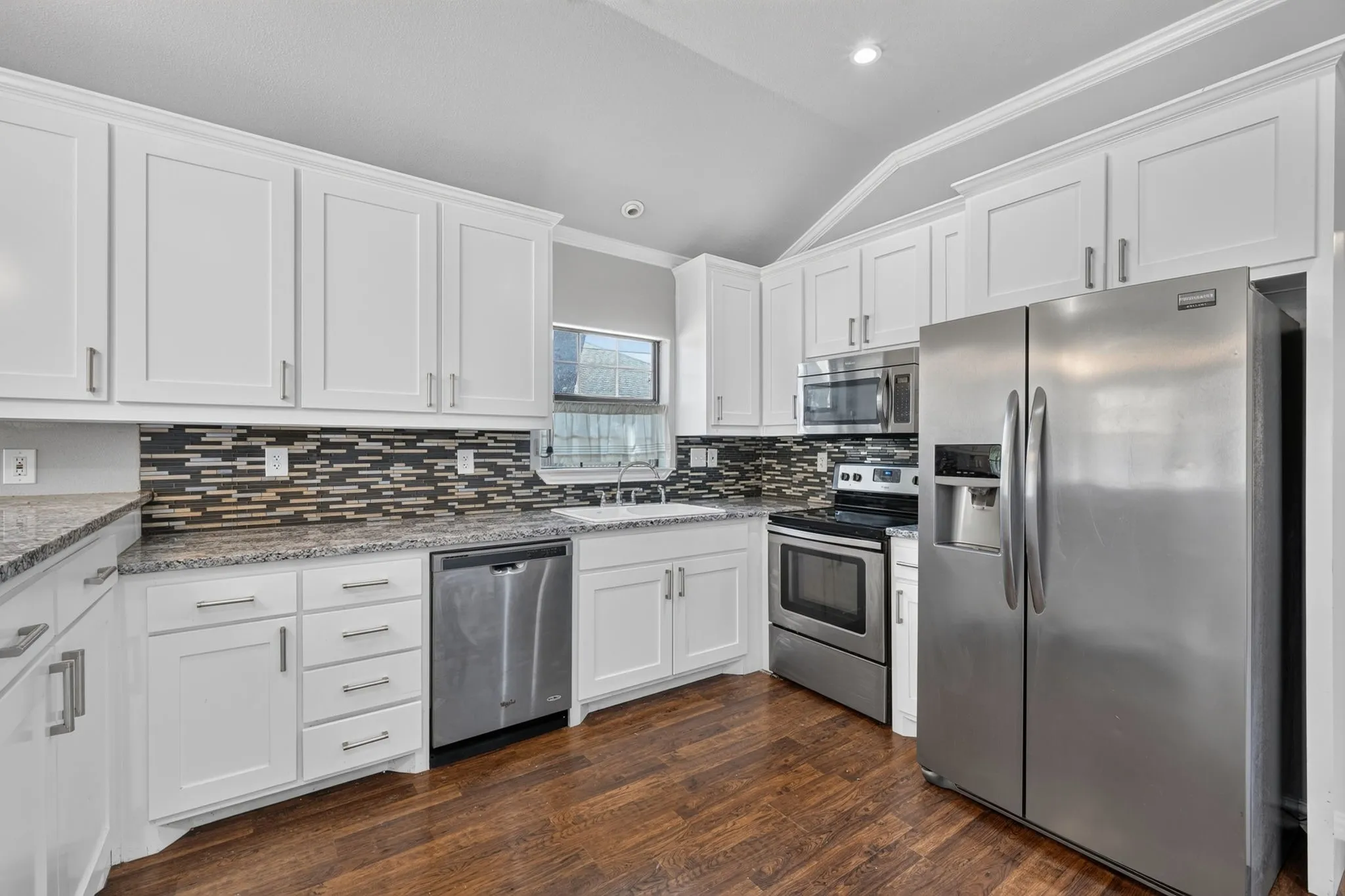 Well-appointed kitchen featuring white cabinetry, stainless steel appliances, granite countertops, a mosaic tile backsplash, and wood- look finish flooring