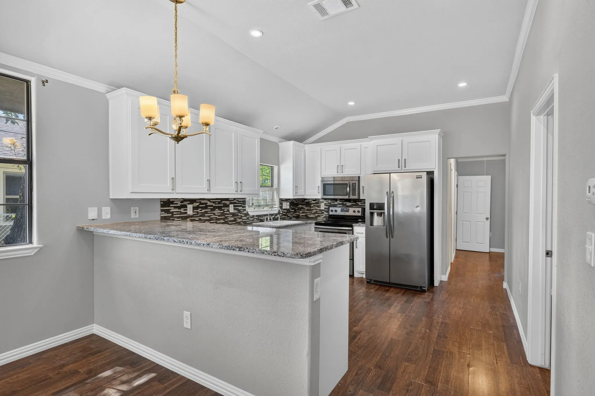Kitchen featuring white cabinetry, stainless steel appliances, granite countertops, and a mosaic tile backsplash