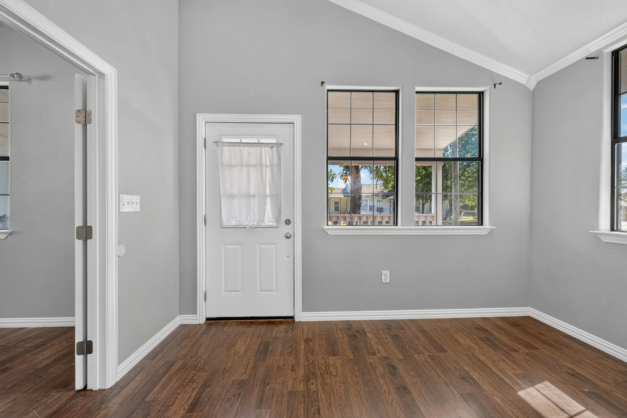 Wood-look finish flooring, vaulted ceiling, light gray wall paint, multiple pane windows, and white trim throughout