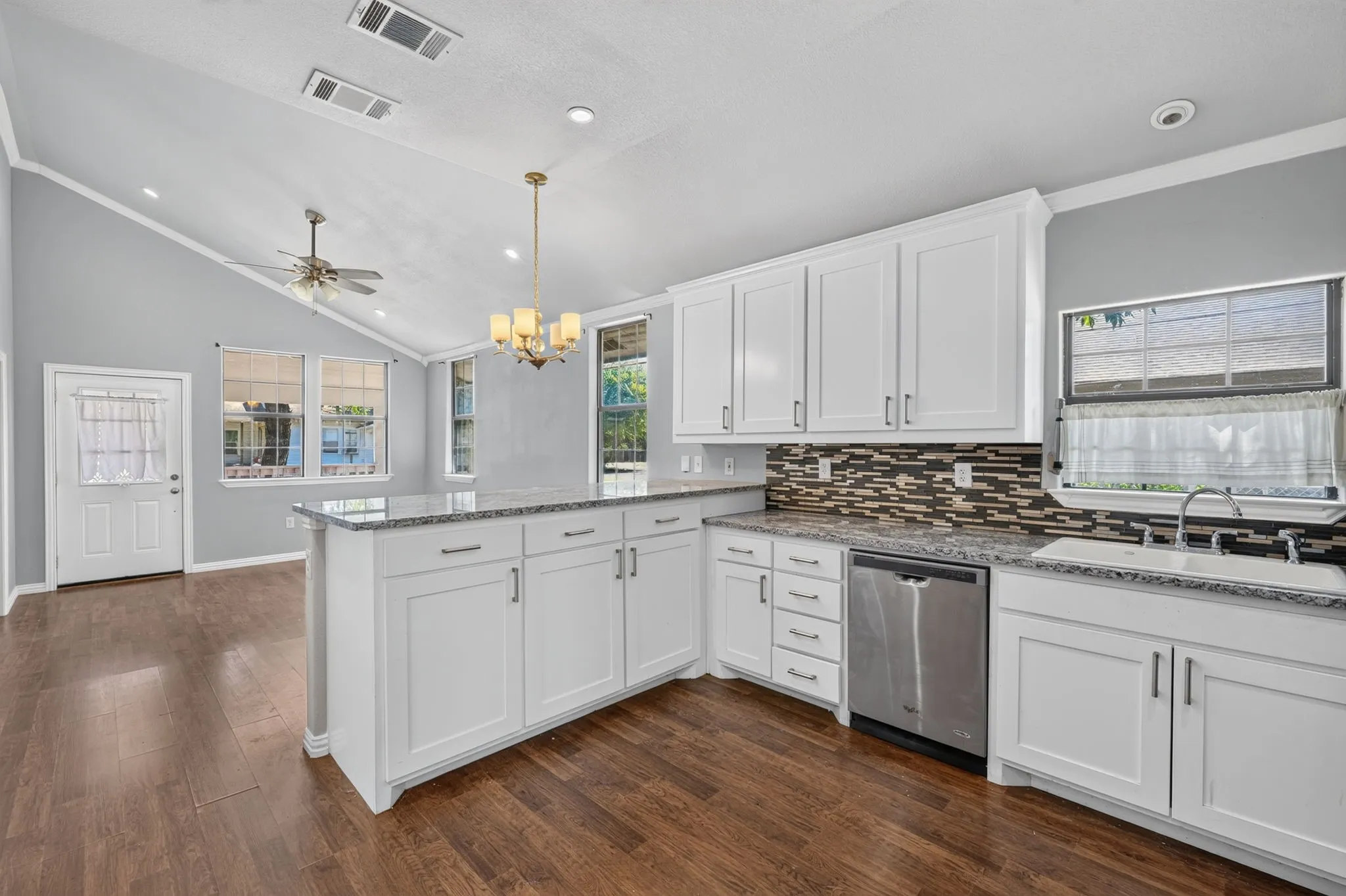 Kitchen with white shaker cabinetry, stainless steel dishwasher, speckled countertops, and a mosaic tile backsplash
