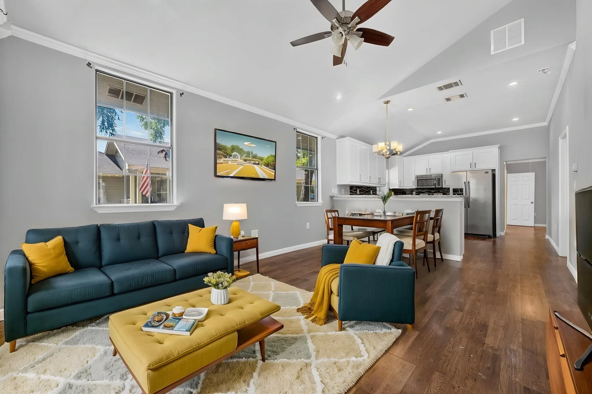 Vaulted ceiling, wood-look finish flooring, white cabinetry, stainless steel appliances, and ceiling fan