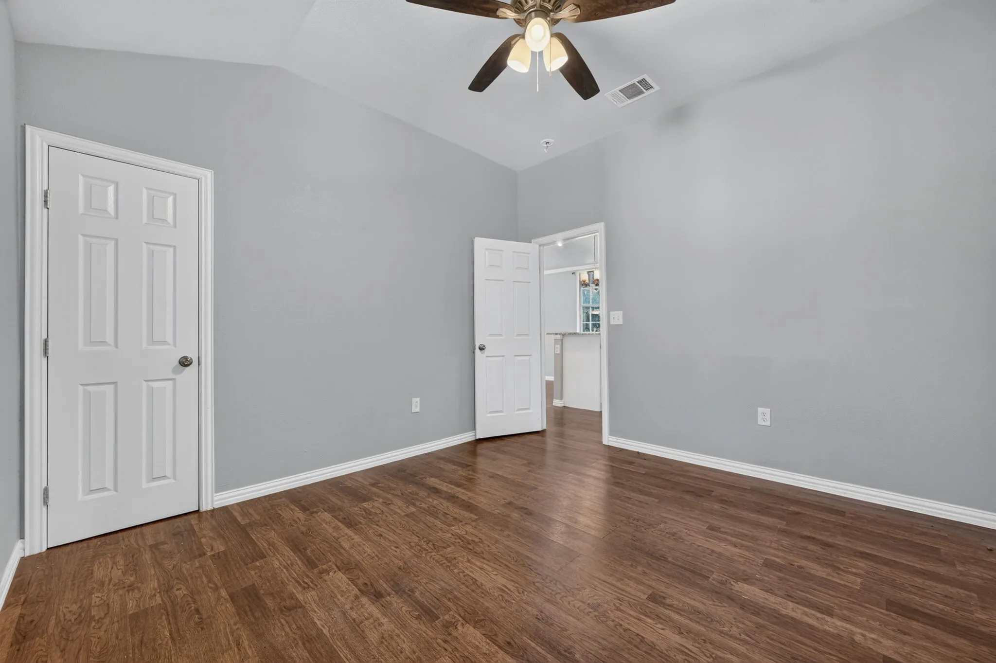 Wood look-finish flooring with light gray walls, vaulted ceiling, and a ceiling fan