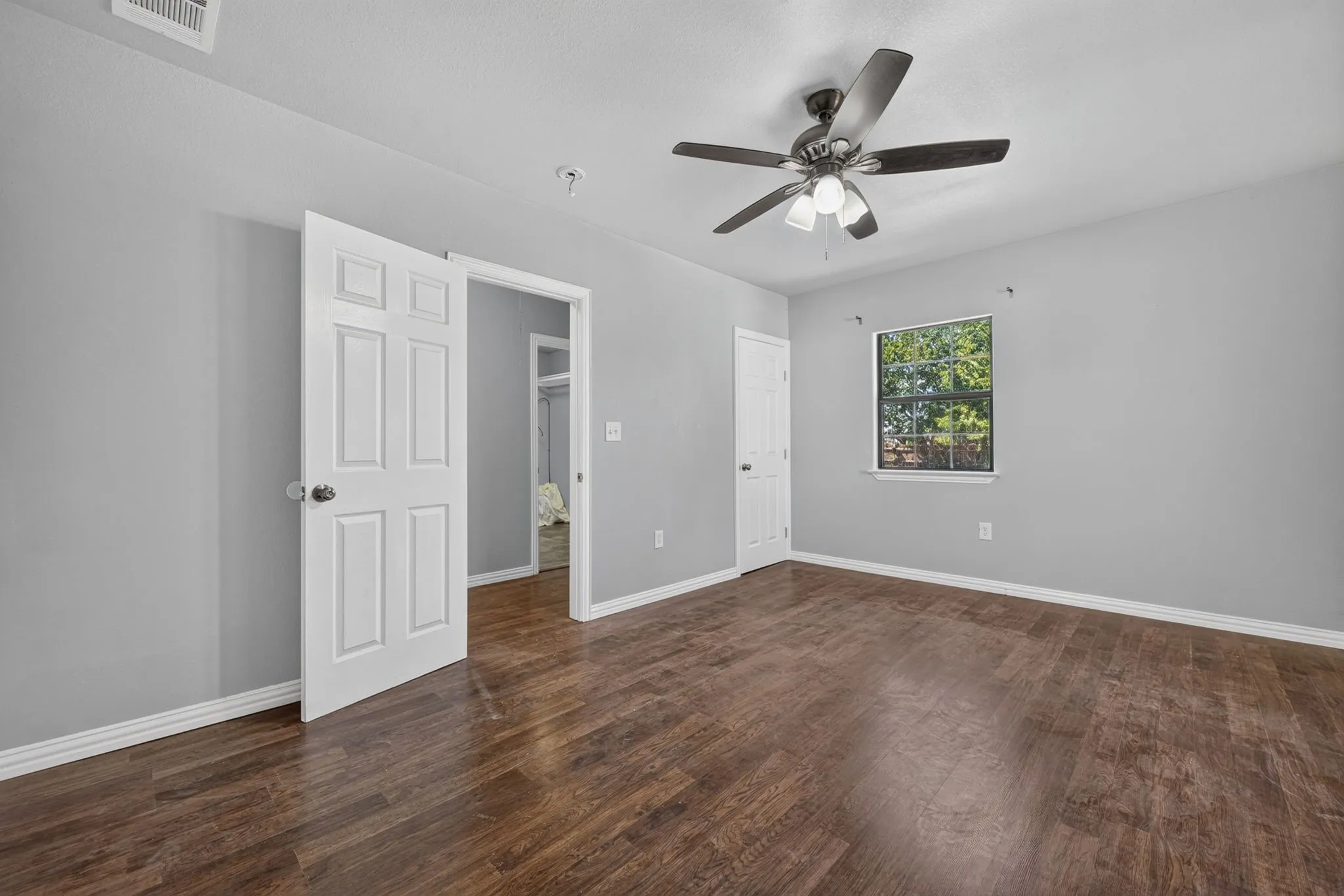 Wood look finish flooring, light gray walls, white trim, ceiling fan with integrated lighting, and a window with exterior visibility