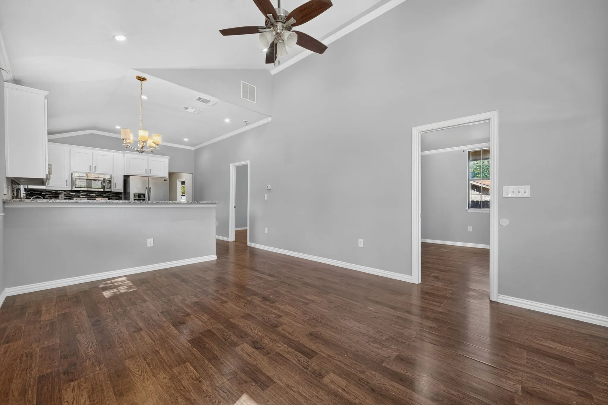 Vaulted ceilings, wood-look finish flooring, white cabinetry, stainless steel appliances, and a ceiling fan with integrated lighting