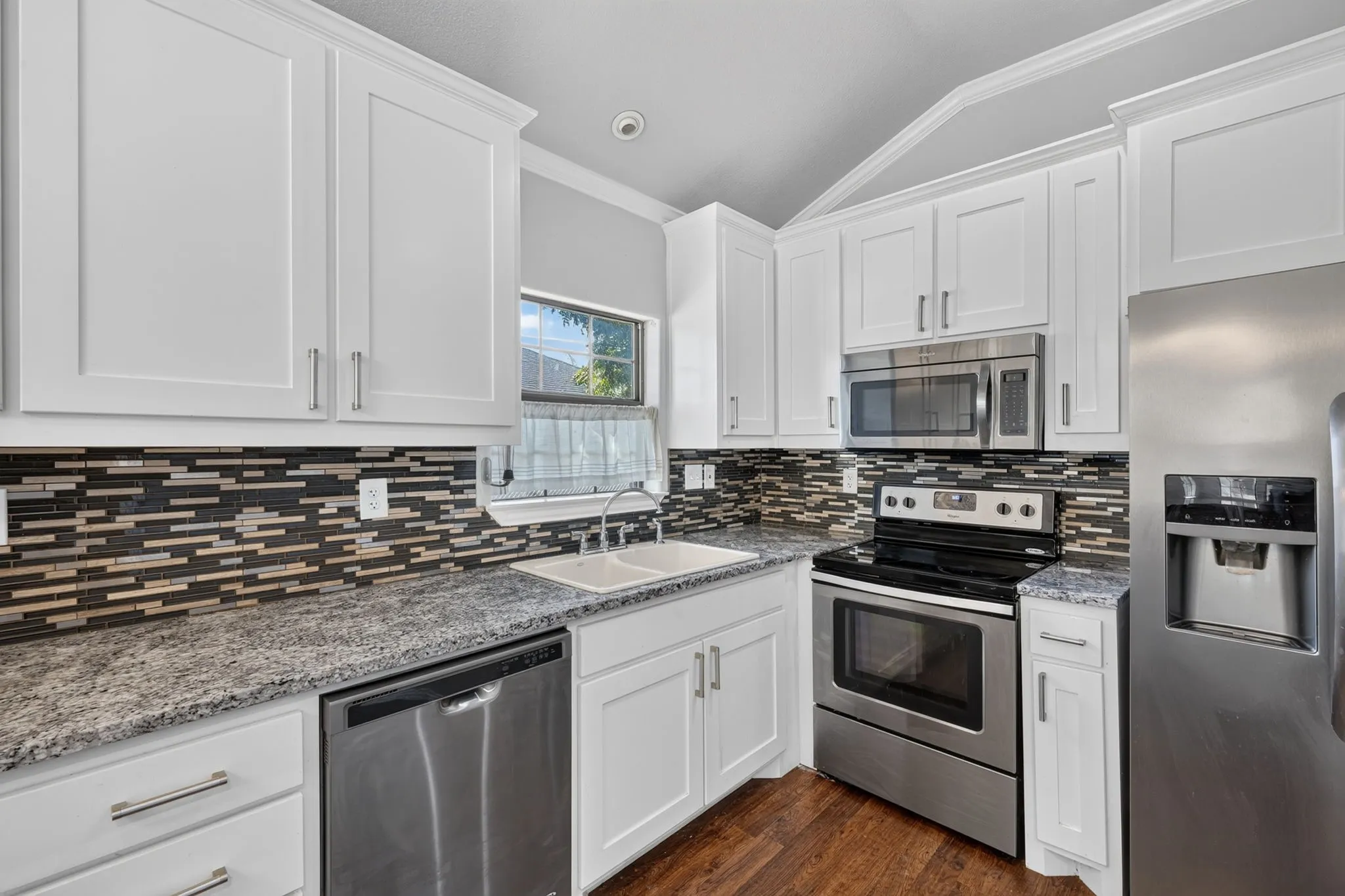 Kitchen featuring white shaker-style cabinetry, stainless steel appliances, granite countertops, a mosaic tile backsplash, and wood-look finish flooring