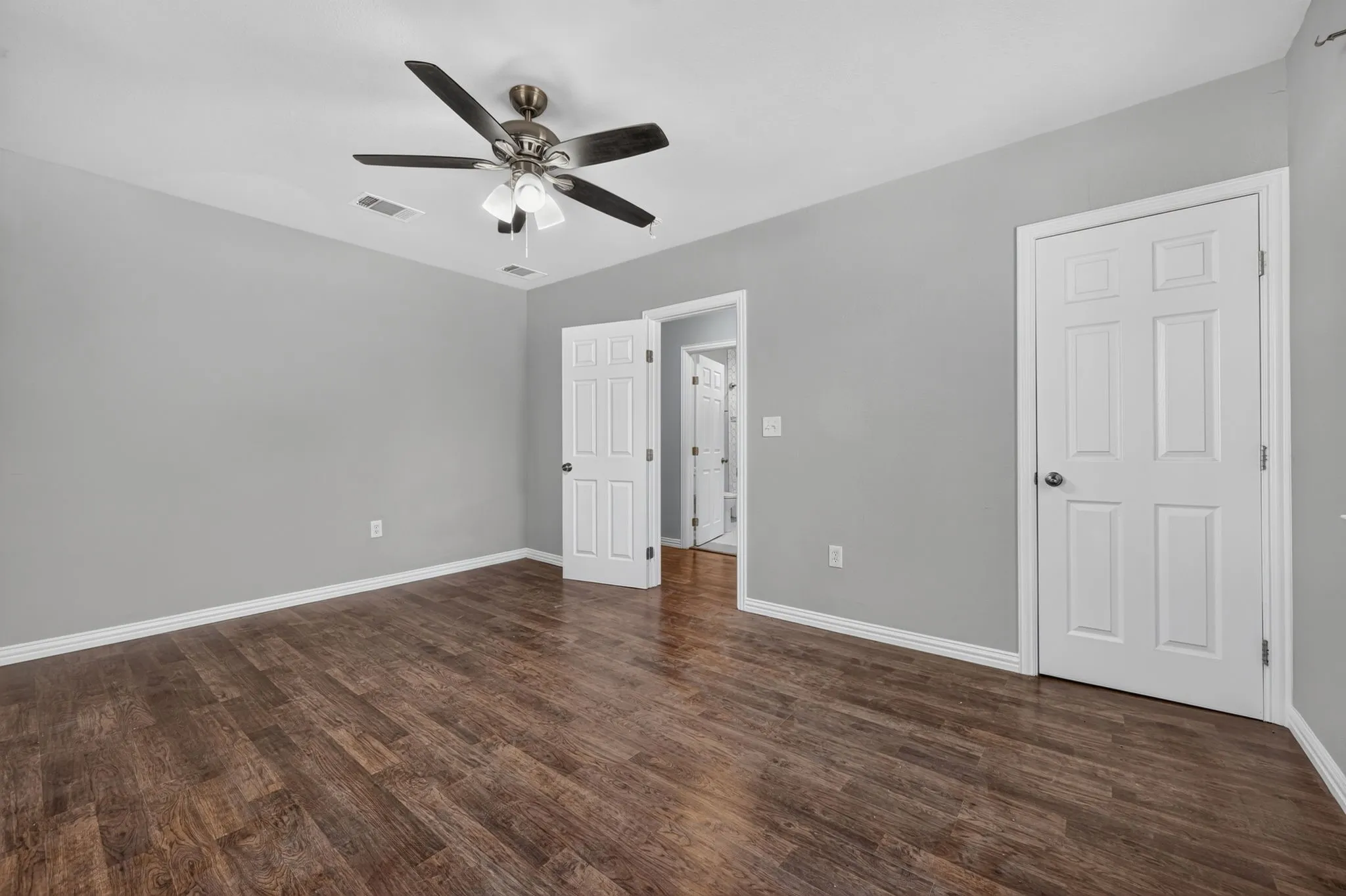 Spacious room featuring rich wood-look finish flooring, light gray wall paint, a ceiling fan with integrated lighting, and white paneled doors