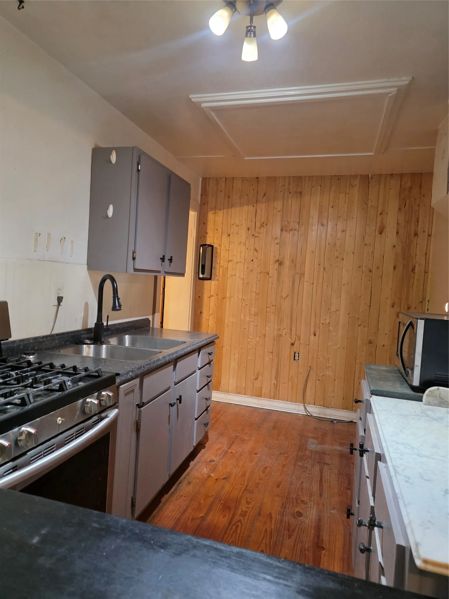 Wood-finish flooring with light grey cabinetry, a stainless steel gas range, and a dual basin sink with a matte black faucet