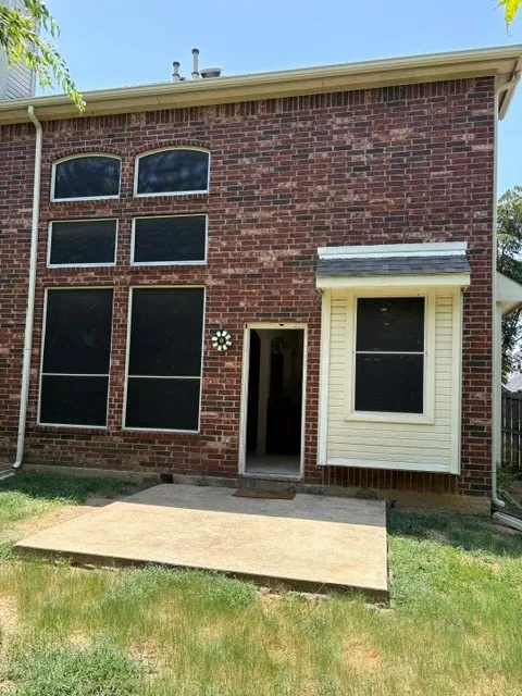 Brick exterior featuring a concrete patio, multiple windows with solar screens, and an awning over a lower-level window