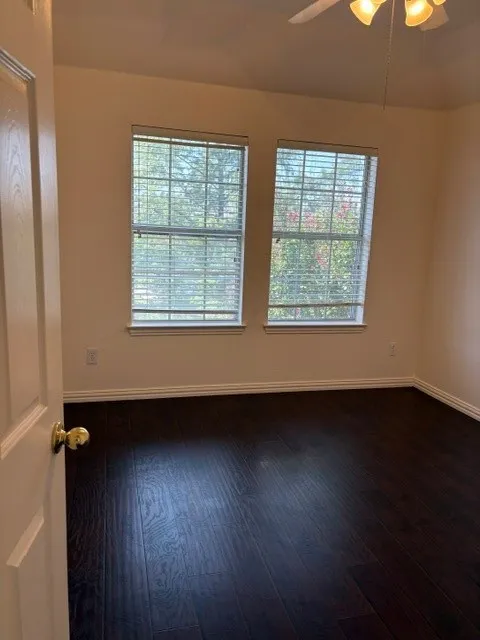 Spacious room featuring dark wood-finish flooring and two large windows with blinds