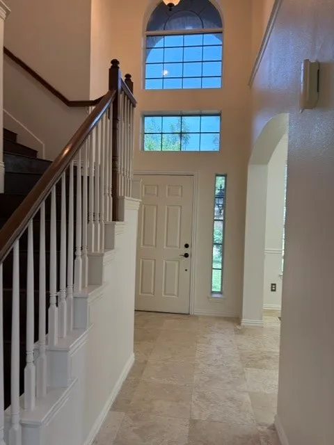 Two-story entry featuring light-toned tile flooring, a multi-pane arched window, and a grand staircase with dark wood handrails and white balusters