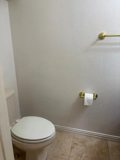 Neutral-toned walls featuring a toilet with a white seat, complemented by brass-finish fixtures and stone tile flooring