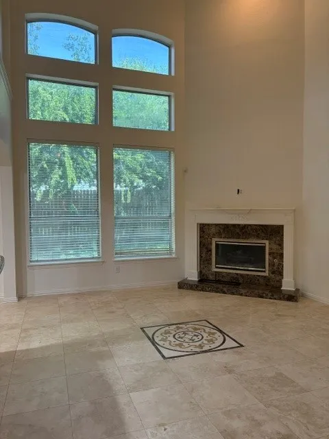 Two-story living area featuring a corner fireplace with a stone surround and mantel, a floor-to-ceiling window arrangement with arched transoms, and large format tile flooring with a central decorative inlay