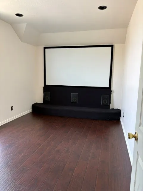 Dedicated media room featuring a large projection screen, integrated speakers, and dark wood-finish flooring