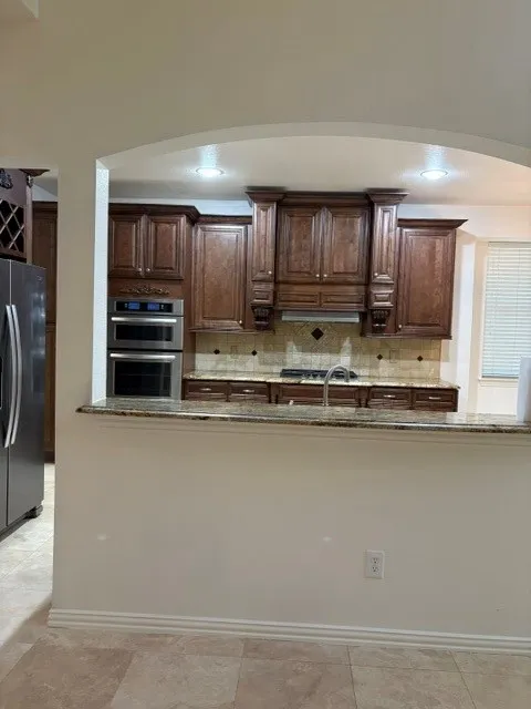 Kitchen featuring rich wood cabinetry, stainless steel double ovens, granite countertops, and a tiled backsplash