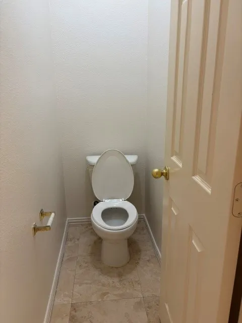 White toilet with a round bowl, set against light-colored walls and complemented by textured tile flooring