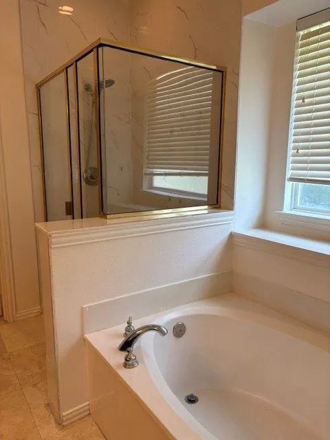 Bathroom featuring a built-in soaking tub with polished chrome fixtures, a separate glass-enclosed shower with gold-tone framing, and a window with horizontal blinds