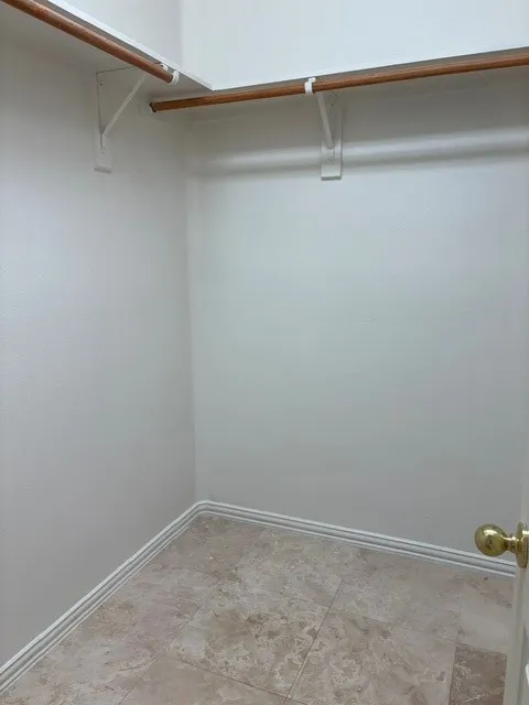 Walk-in closet featuring tile flooring, white baseboards, white walls, and wood-finish hanging rods with shelving
