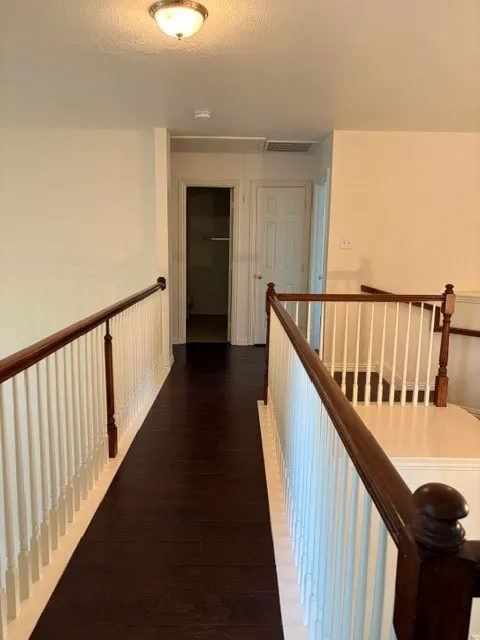 Upper-level hallway featuring dark wood-finish flooring, white balusters, and a wooden handrail