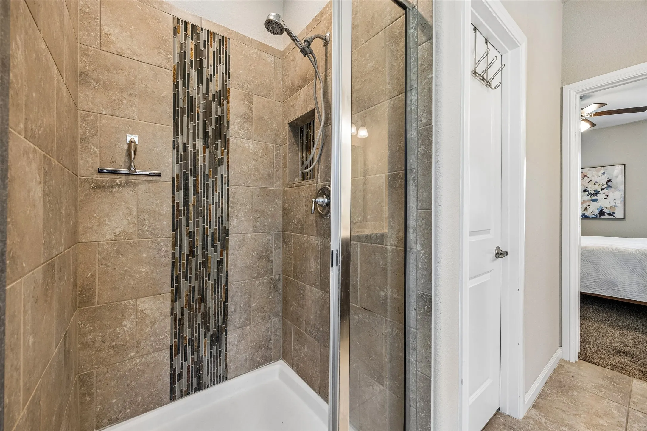 Spa-inspired shower featuring large-format tile walls, decorative linear tile accent strip, frameless glass enclosure, rainfall showerhead, and tile flooring throughout