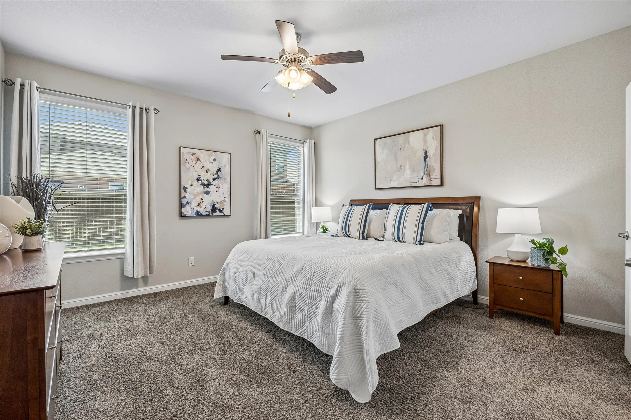Neutral wall paint, textured carpet flooring, ceiling fan with light fixture, and two windows with blinds