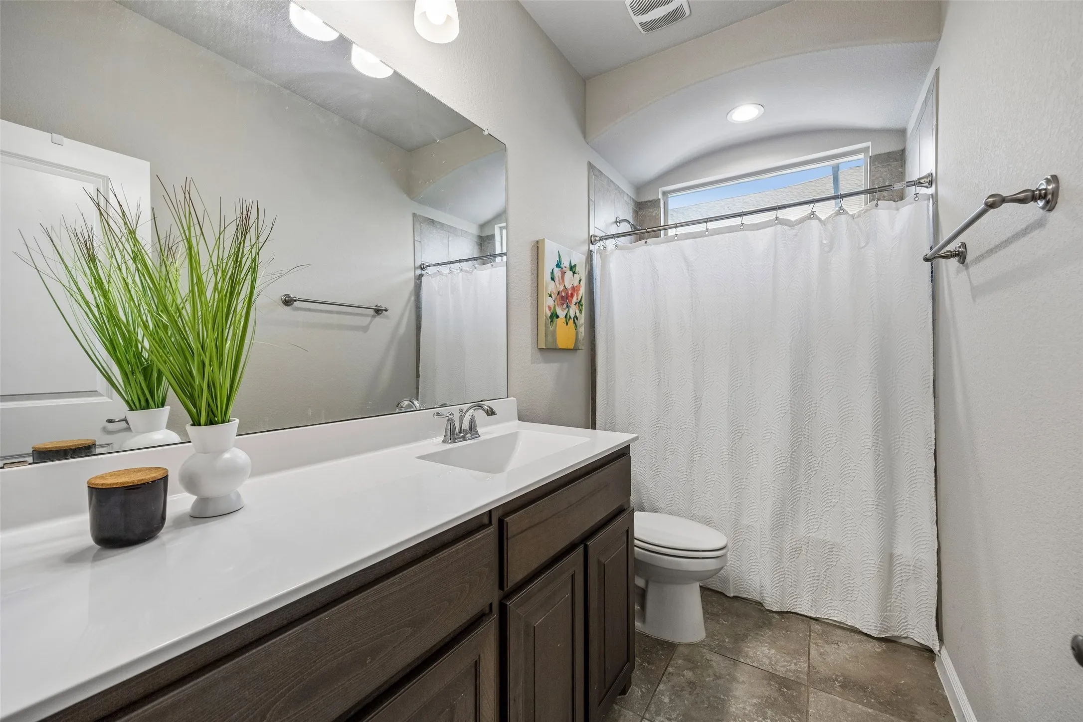 Guest bathroom with dark wood-finish vanity with a white countertop, chrome faucet, wall-mounted mirror, and tile flooring