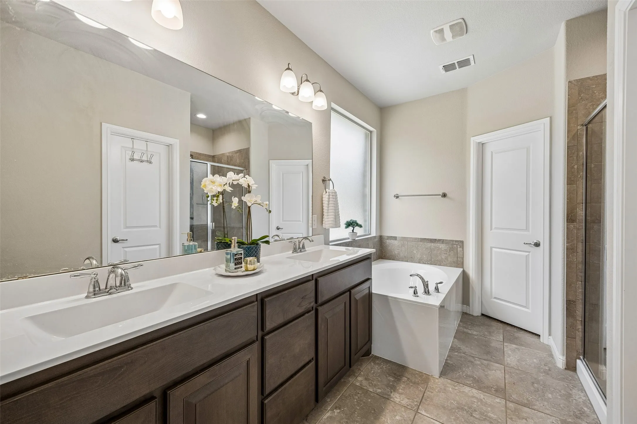 Dual vanity with undermount sinks, an elongated mirror, a built-in bathtub, and a separate glass-enclosed shower