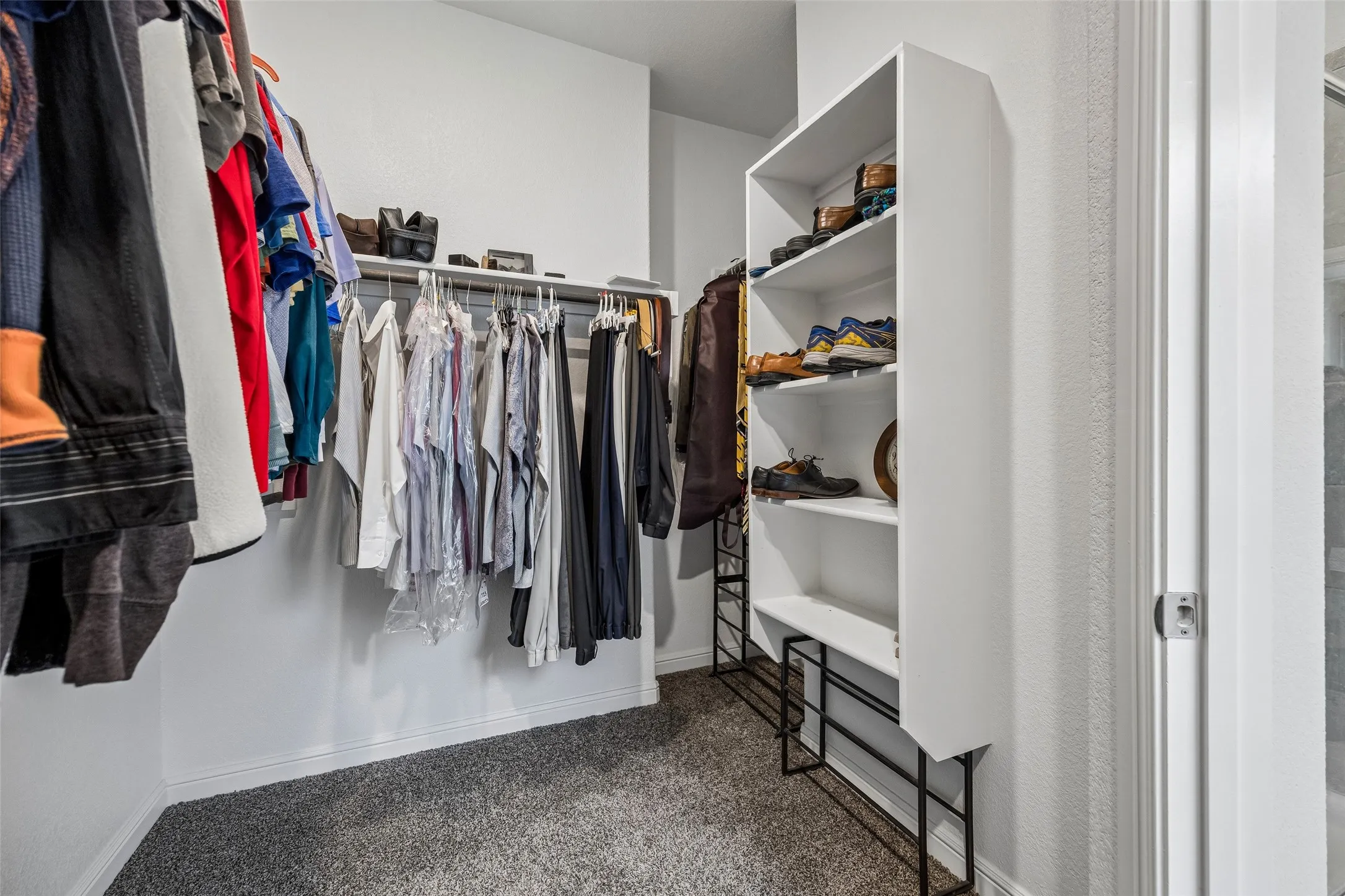 Primary bedroom walk-in closet with built-in shelving unit, clothing rods, and textured wall finish