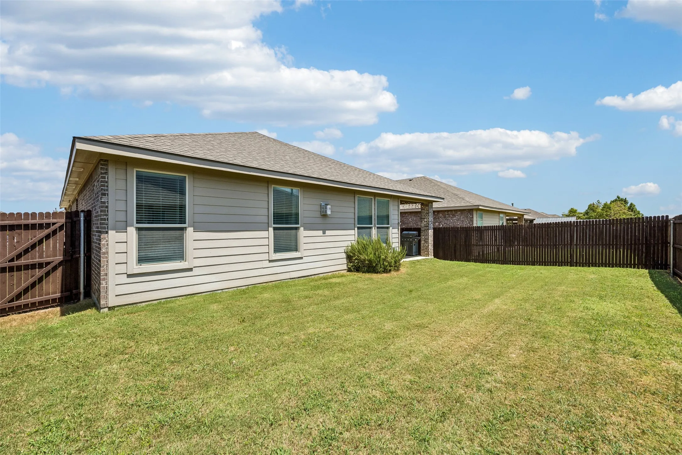 Expansive fenced backyard featuring a manicured lawn, horizontal siding, brick exterior accents, and a shingled roof