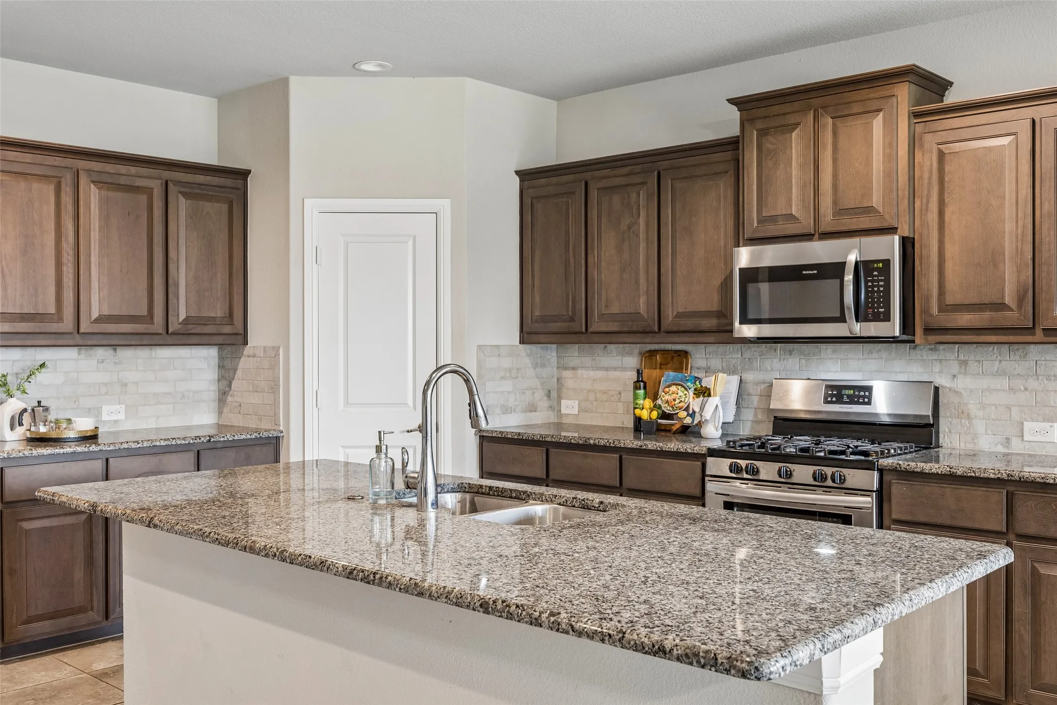 Kitchen featuring a gas range, an island with a stainless steel sink, granite countertops, wood-finish cabinetry and stainless steel microwave