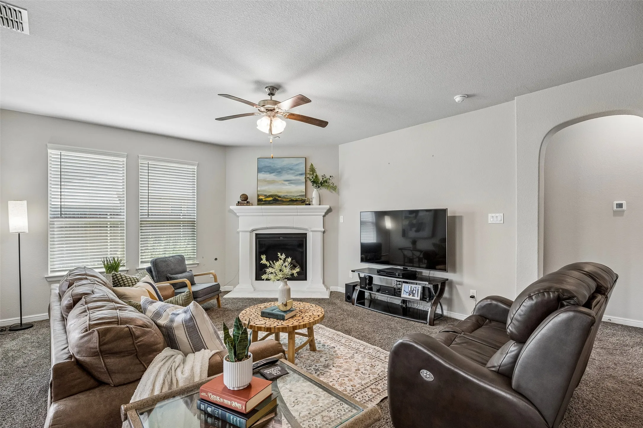 Spacious living room anchored by a fireplace with a decorative mantel, complemented by ceiling fan with integrated lighting