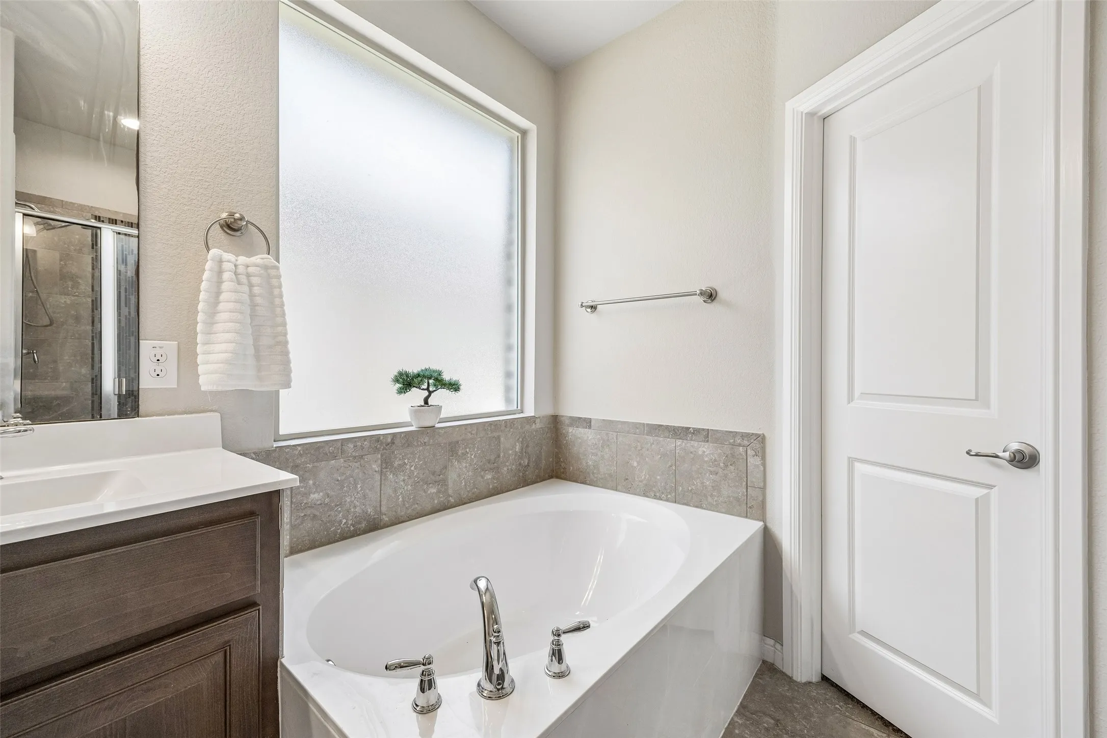 Deep soaking tub with chrome fixtures, tiled surround, and privacy window