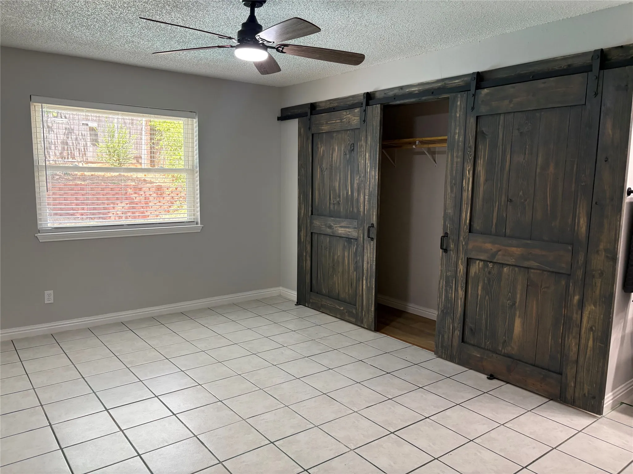 The stylish master features sliding barn doors that access the large closet, tile floor, and an updated ceiling fan.