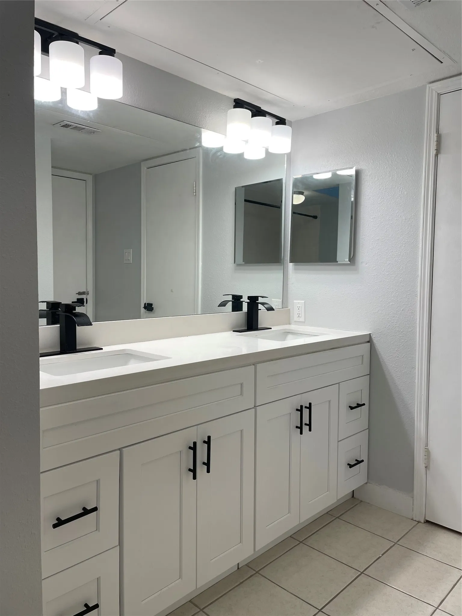 Dual vanity with white shaker-style cabinetry, matte black hardware, and light-toned countertops