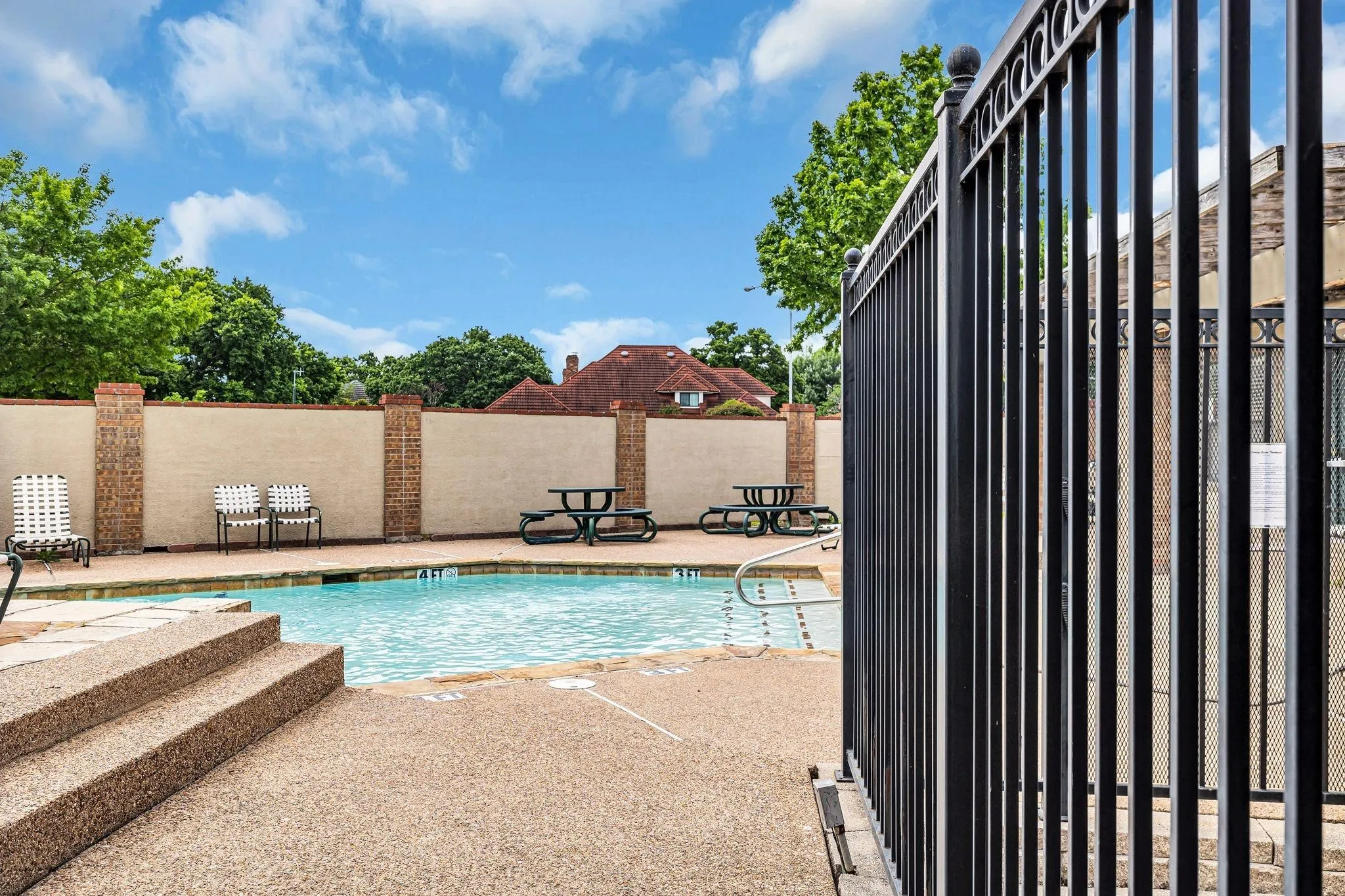 Swimming pool with an exposed aggregate deck, metal handrails, and a surrounding privacy wall with brick pilasters